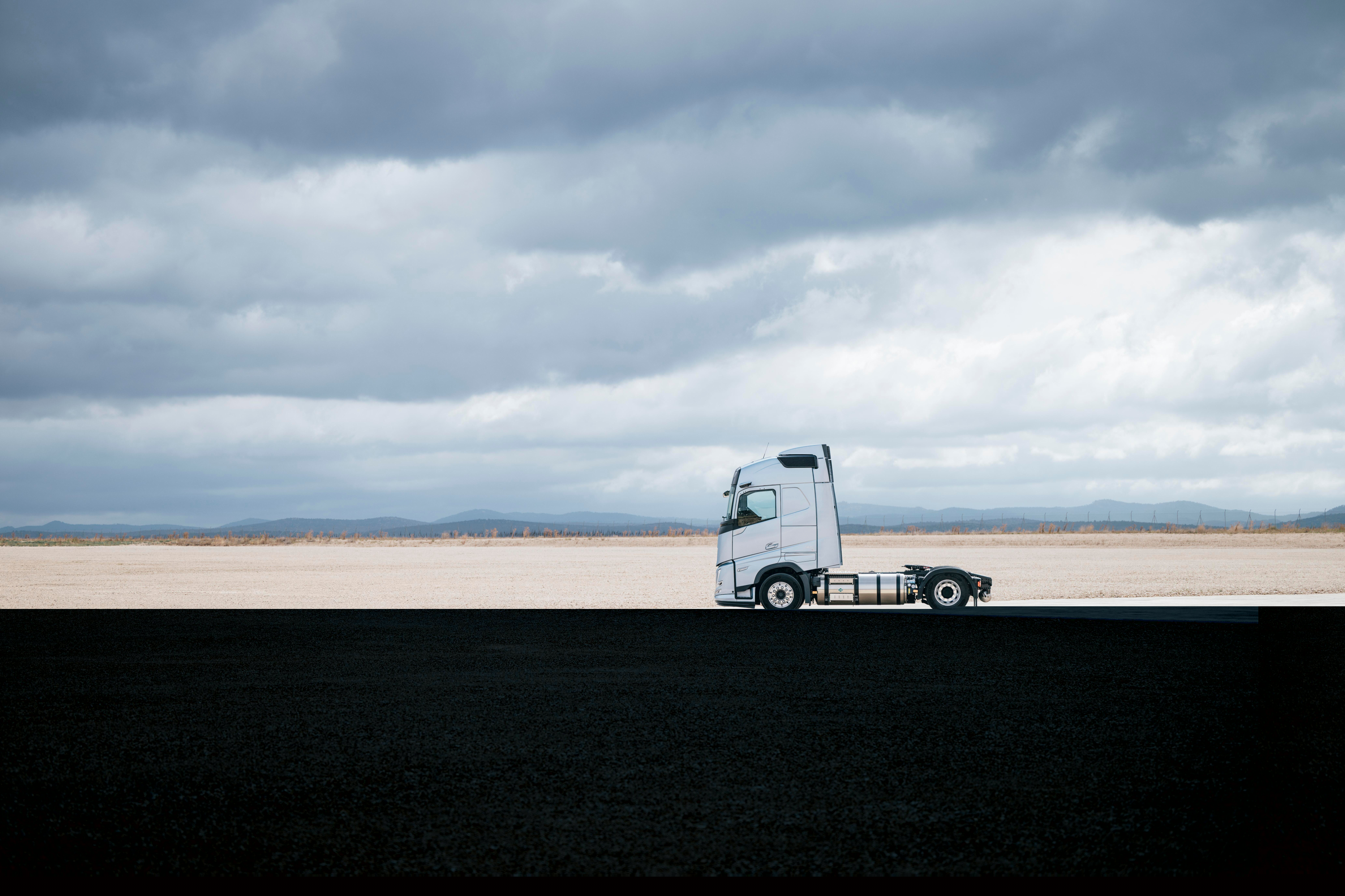 Vue latérale d'un camion Volvo stationné dans un vaste paysage ouvert sous un ciel nuageux, avec des environs immenses et un décor minimal.